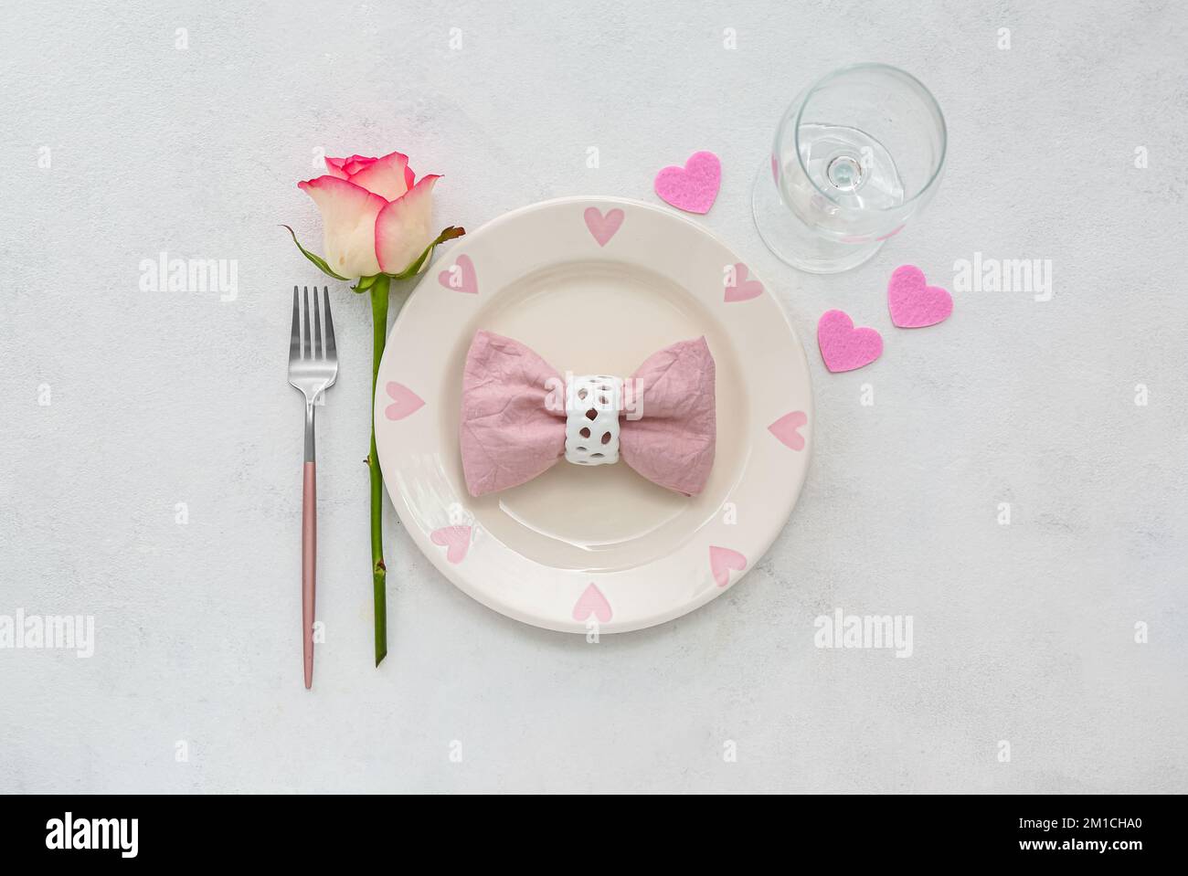 Table setting for Valentine's Day with pink hearts and rose on grey ...