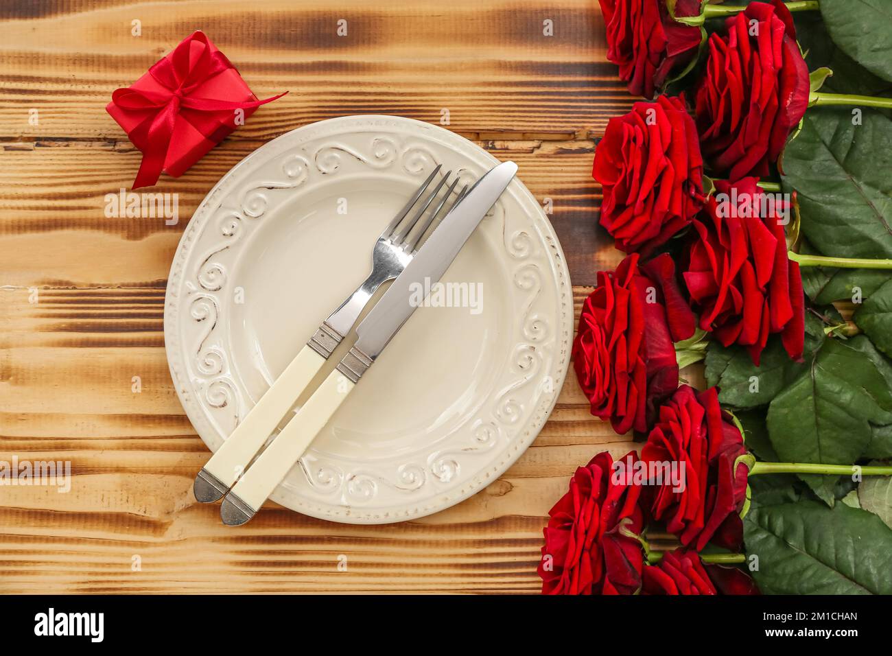 Table setting for Valentine's Day with red roses and gift on wooden ...