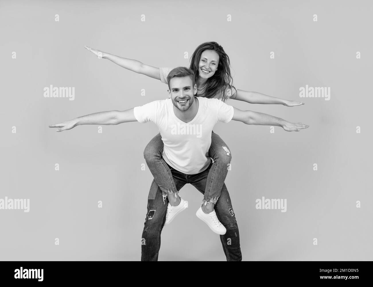 Happy playful woman and man pretend flying doing piggyback ride yellow background, fun Stock Photo