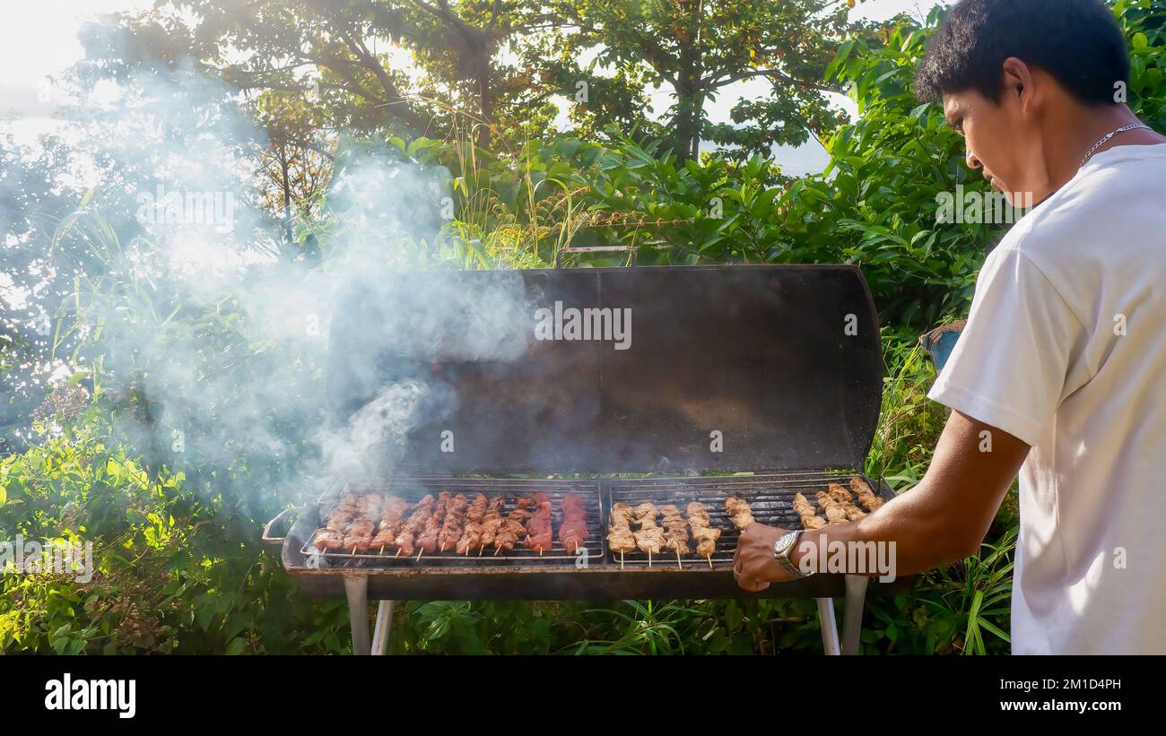 Puerto Galera, Philippines - February 19, 2022. A Filipino man barbecuing meat kebabs, a popular street food in the Philippines. Stock Photo