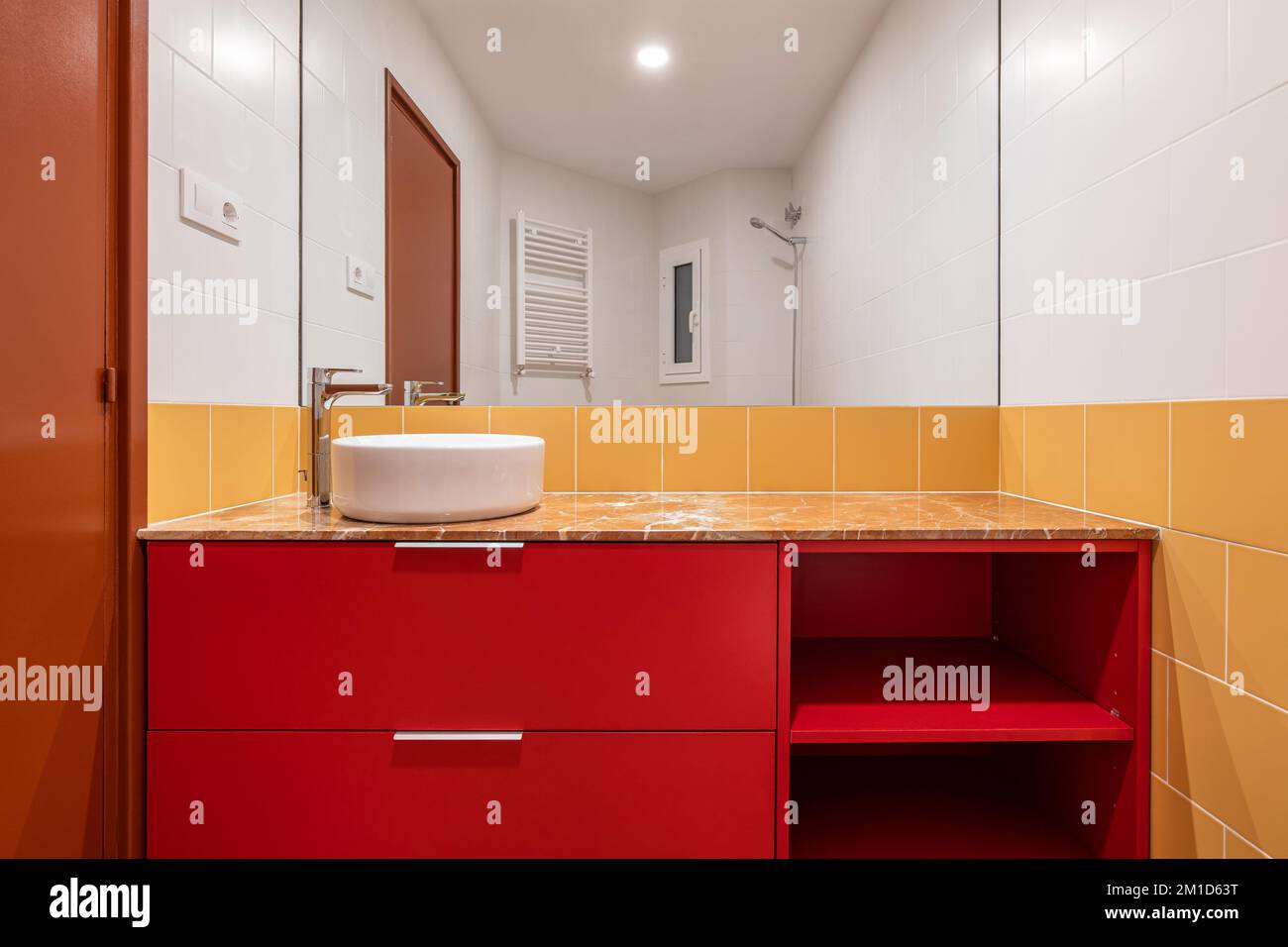 Overhead white sink on a red cabinet in a bright white and yellow bathroom White and yellow tiles on the wall and porcelain stoneware brown floor Stock Photo