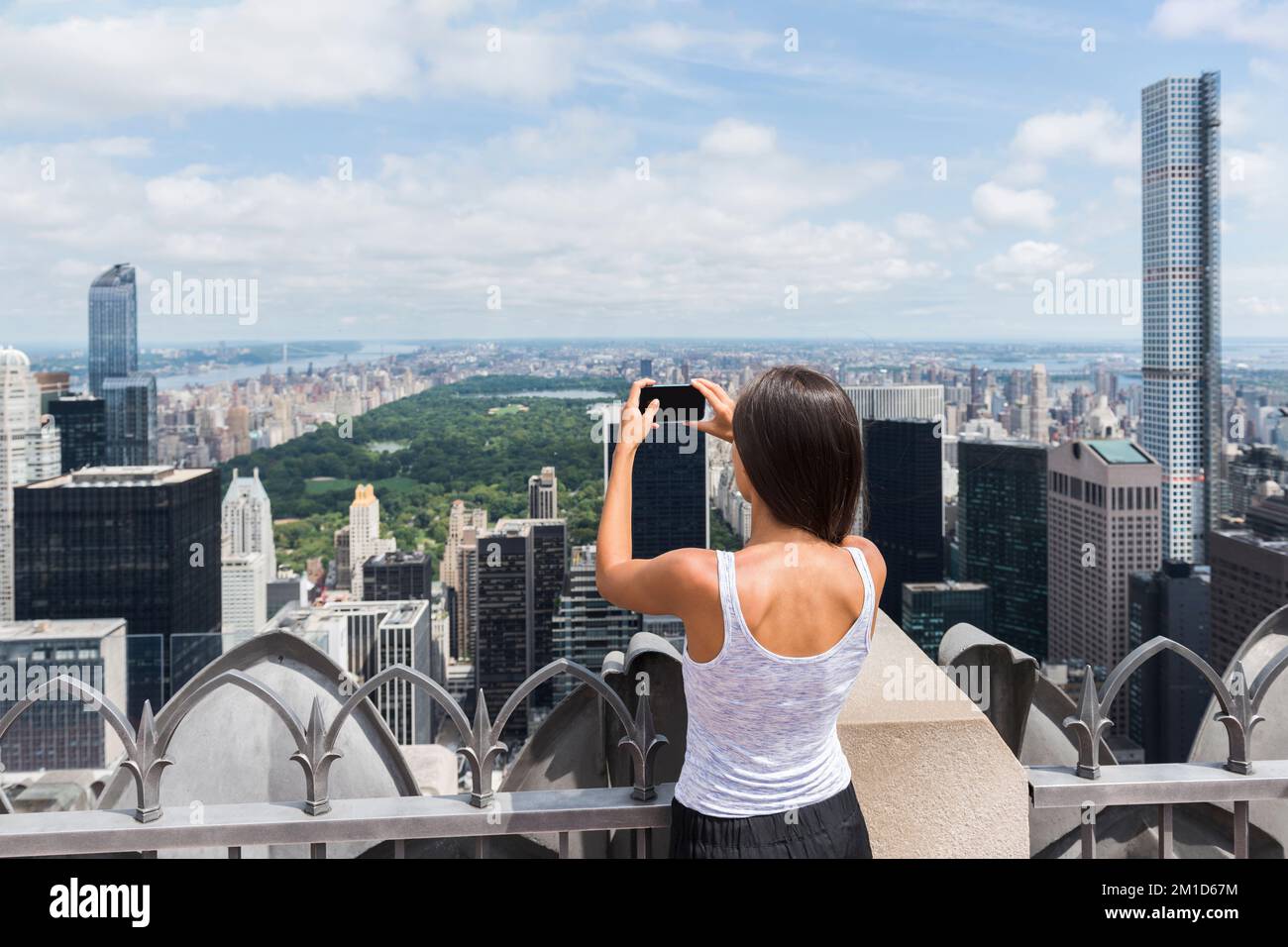 USA travel tourist in New York City vacation- woman looking at view of skyline taking photos with mobile phone from skyscraper. Girl traveling summer Stock Photo