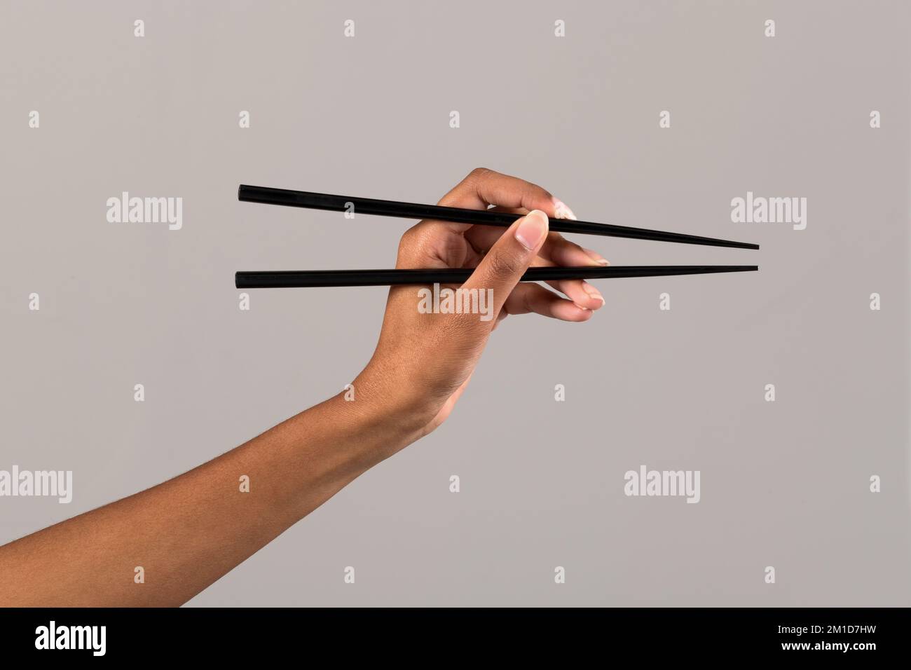 Crop anonymous African American female showing black chopsticks against gray background in studio Stock Photo