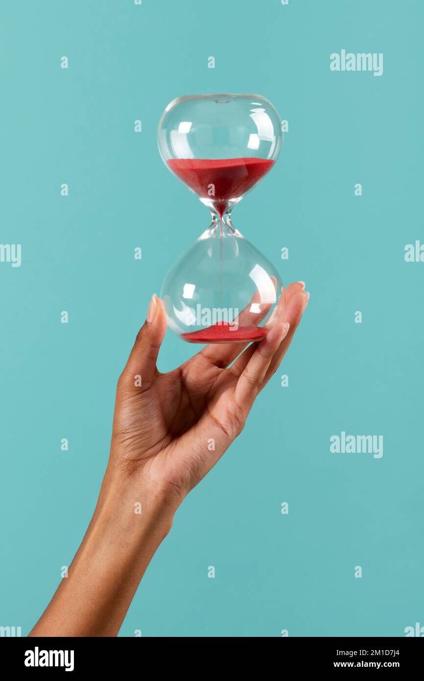 Crop unrecognizable African American female showing hourglass with red sand against turquoise background Stock Photo