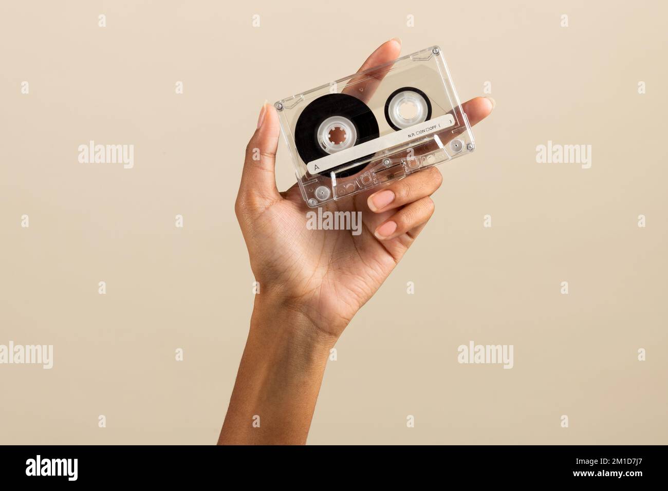 Crop anonymous African American female demonstrating vintage retro cassette tape on beige background Stock Photo