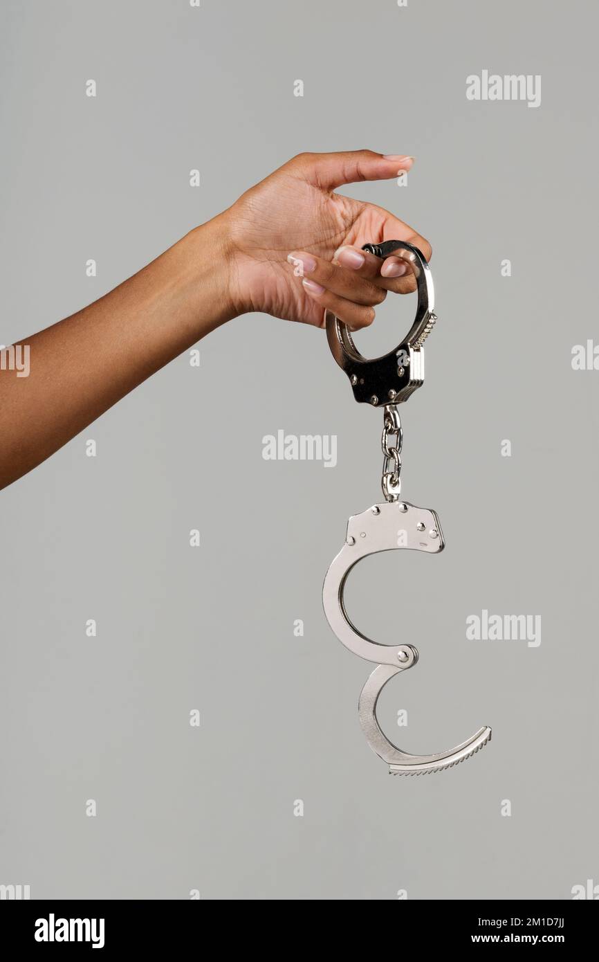 Crop anonymous African American female demonstrating open metal police handcuffs on gray background Stock Photo