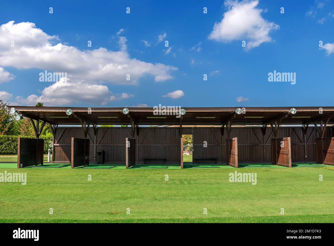 Shed with partitions located near grassy lawn against cloudy blue sky on driving range of golf course Stock Photo
