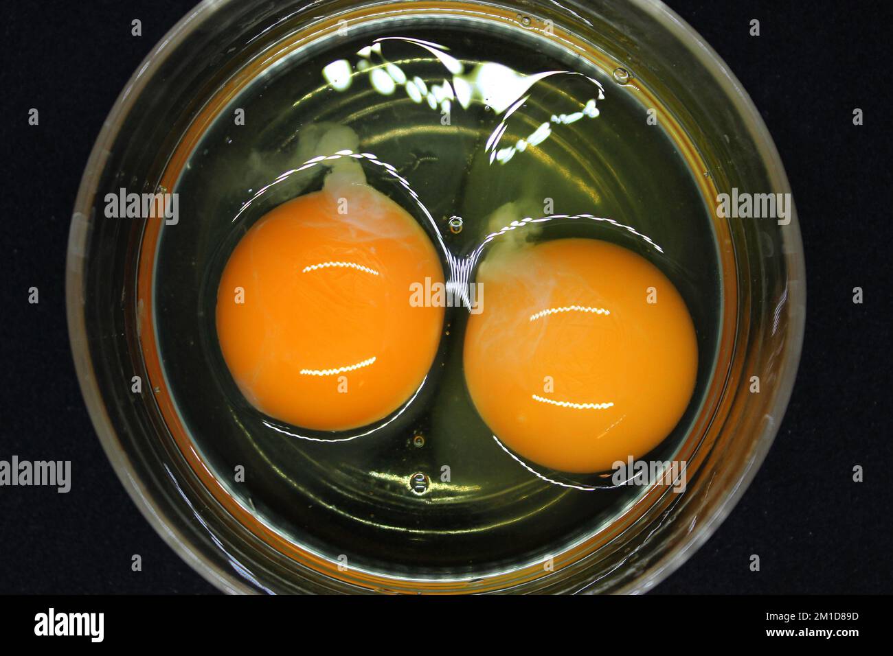 Glare from a kitchen light on two raw eggs with whole yolks cooking