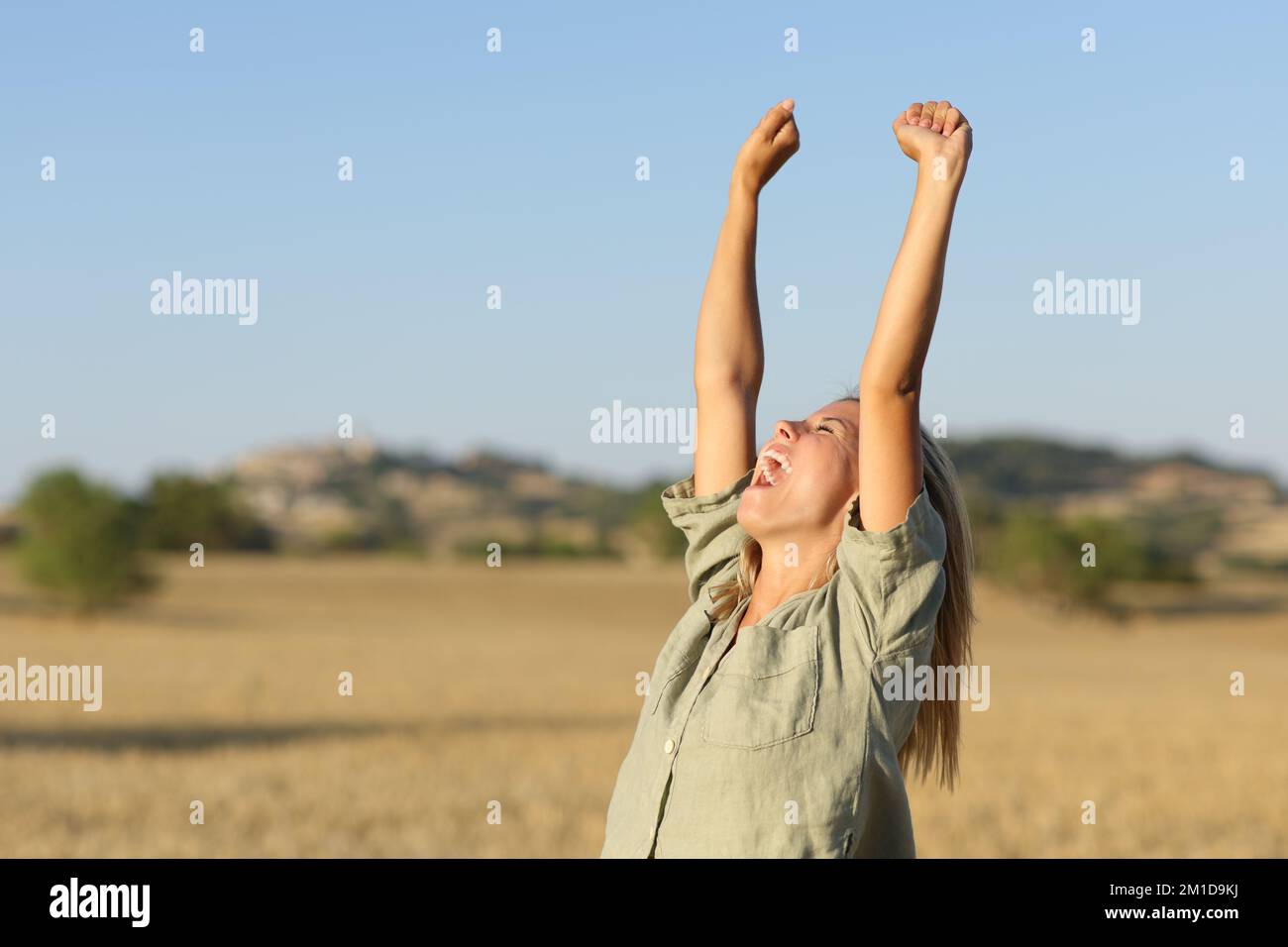 Teen raising arms in a golden wheat field at sunset Stock Photo