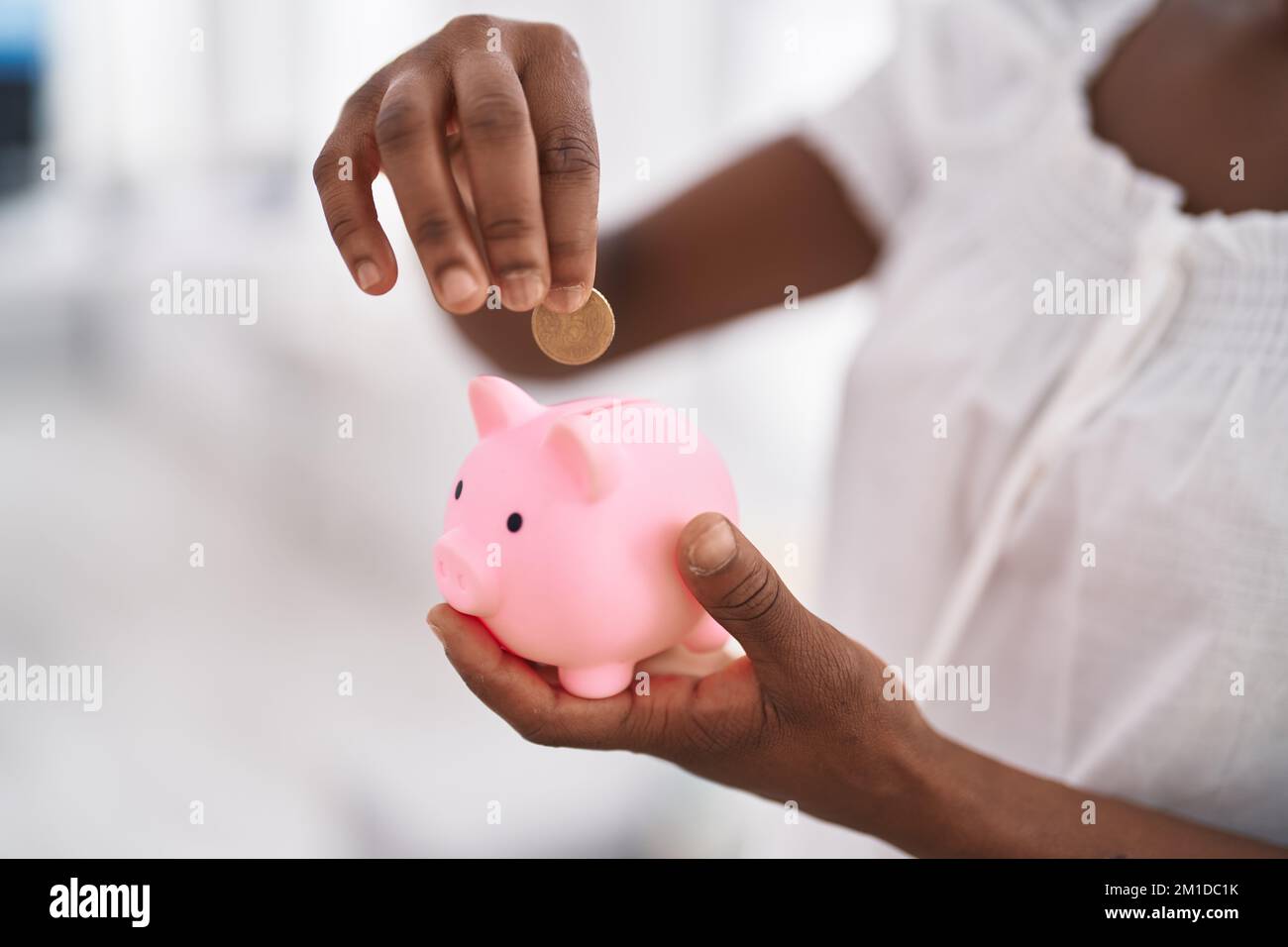 African american woman inserting coin on piggy bank at home Stock Photo ...