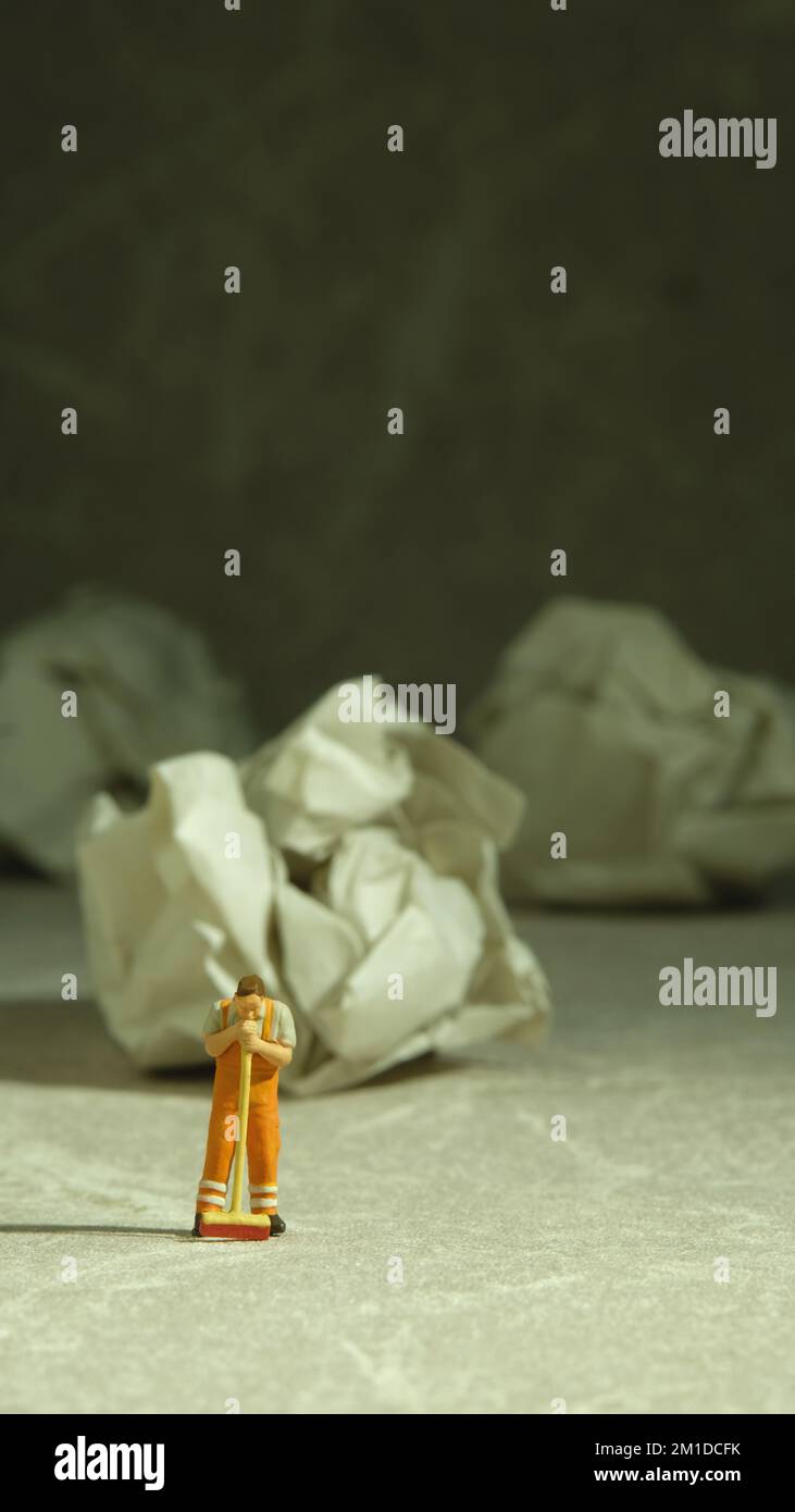 Miniature people toy figure photography. Tired sweeper standing in front of crumple ball of paper on the floor. Image photo Stock Photo