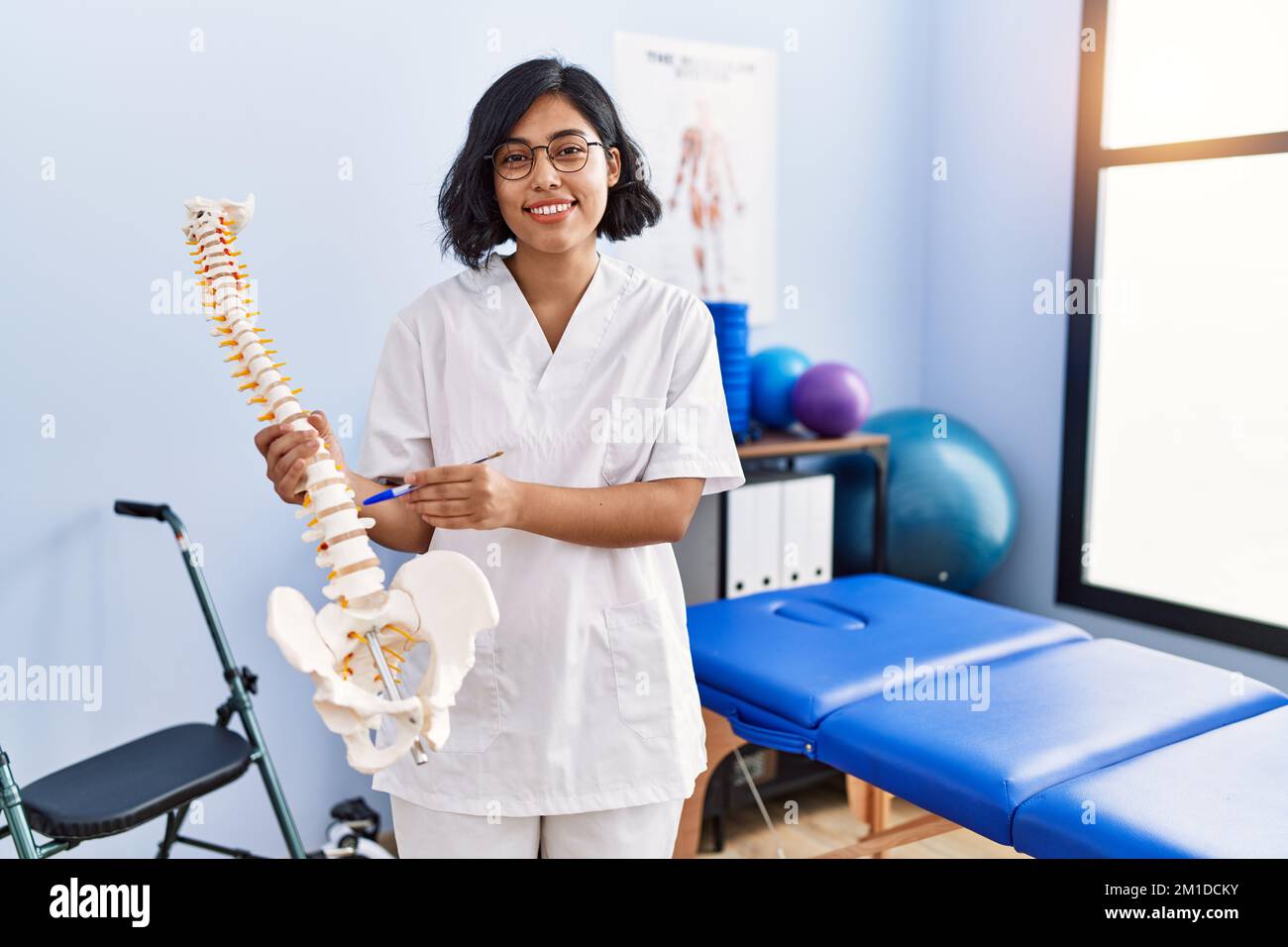 Young latin woman wearing physiotherapist uniform holding anatomical