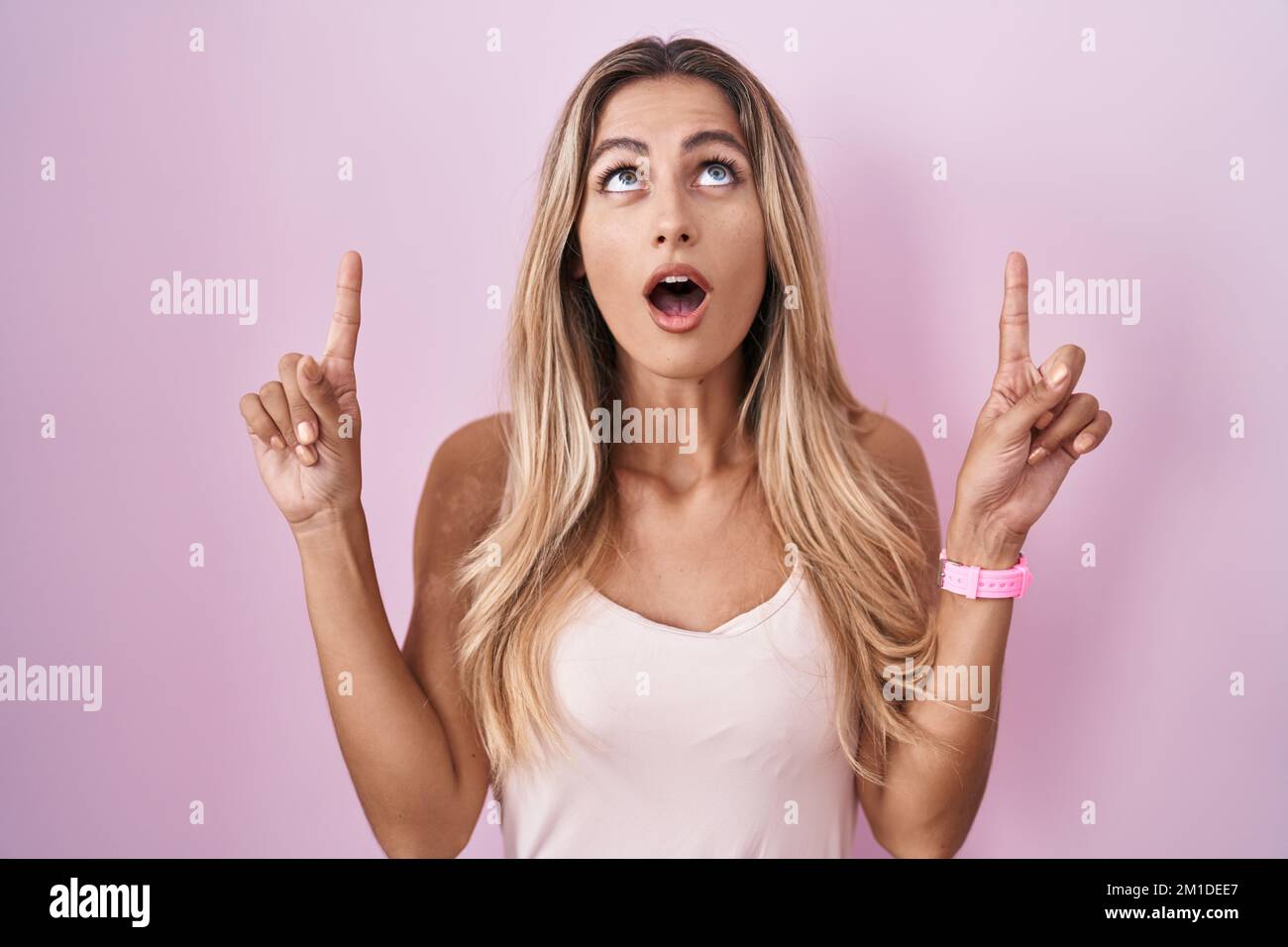 Young blonde woman standing over pink background amazed and surprised ...