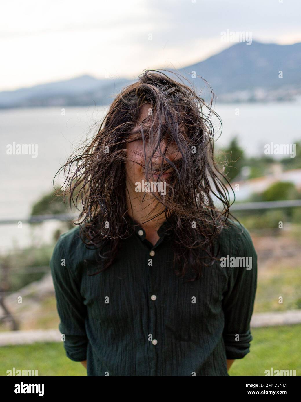 A portrait of a young man with long curly hair posing in a park during the wind Stock Photo