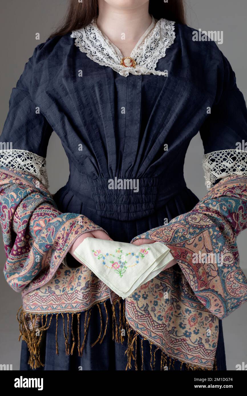 A Victorian woman wearing a blue cotton dress and paisley shawl and holding an embroidered handkerchief Stock Photo