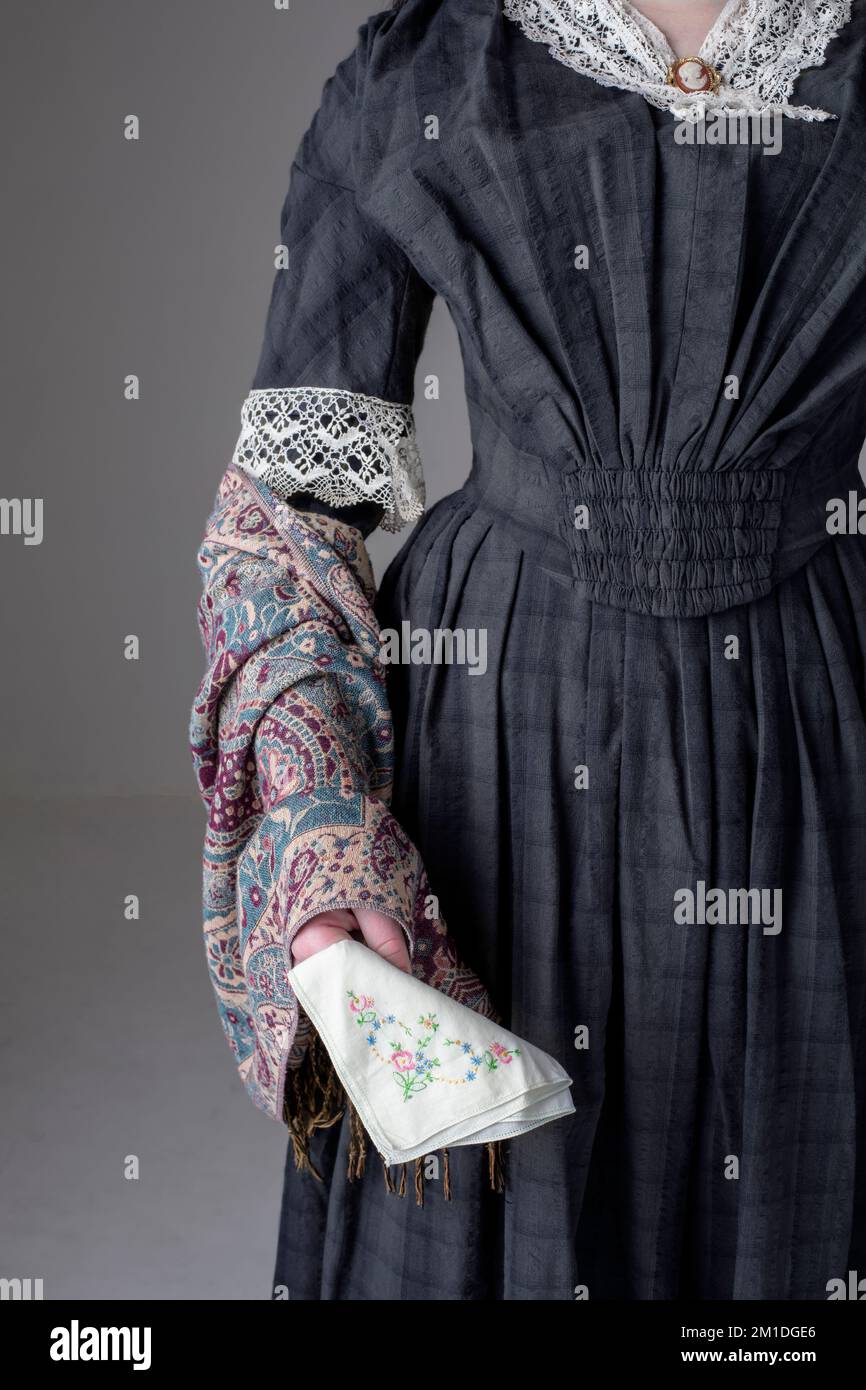 A Victorian woman wearing a blue cotton dress and paisley shawl and holding an embroidered handkerchief Stock Photo