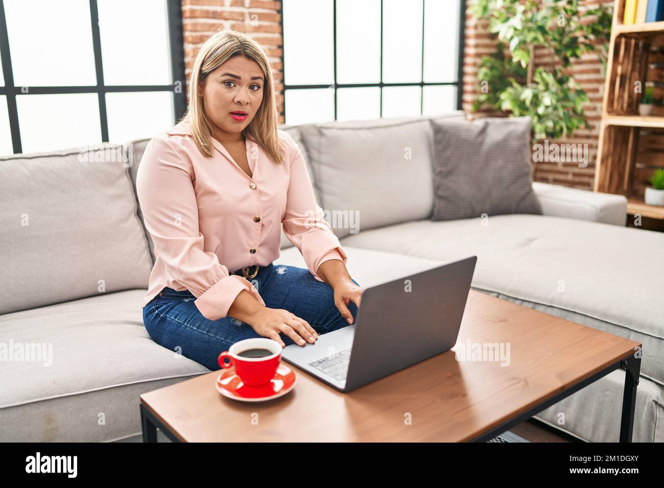Young hispanic woman using laptop sitting on the sofa at home afraid ...