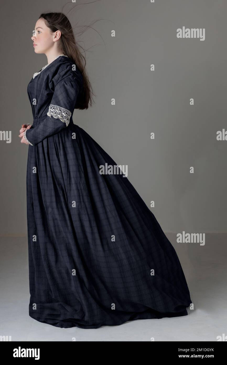 A young Victorian woman wearing a blue cotton dress with lace trim against a studio backdrop Stock Photo
