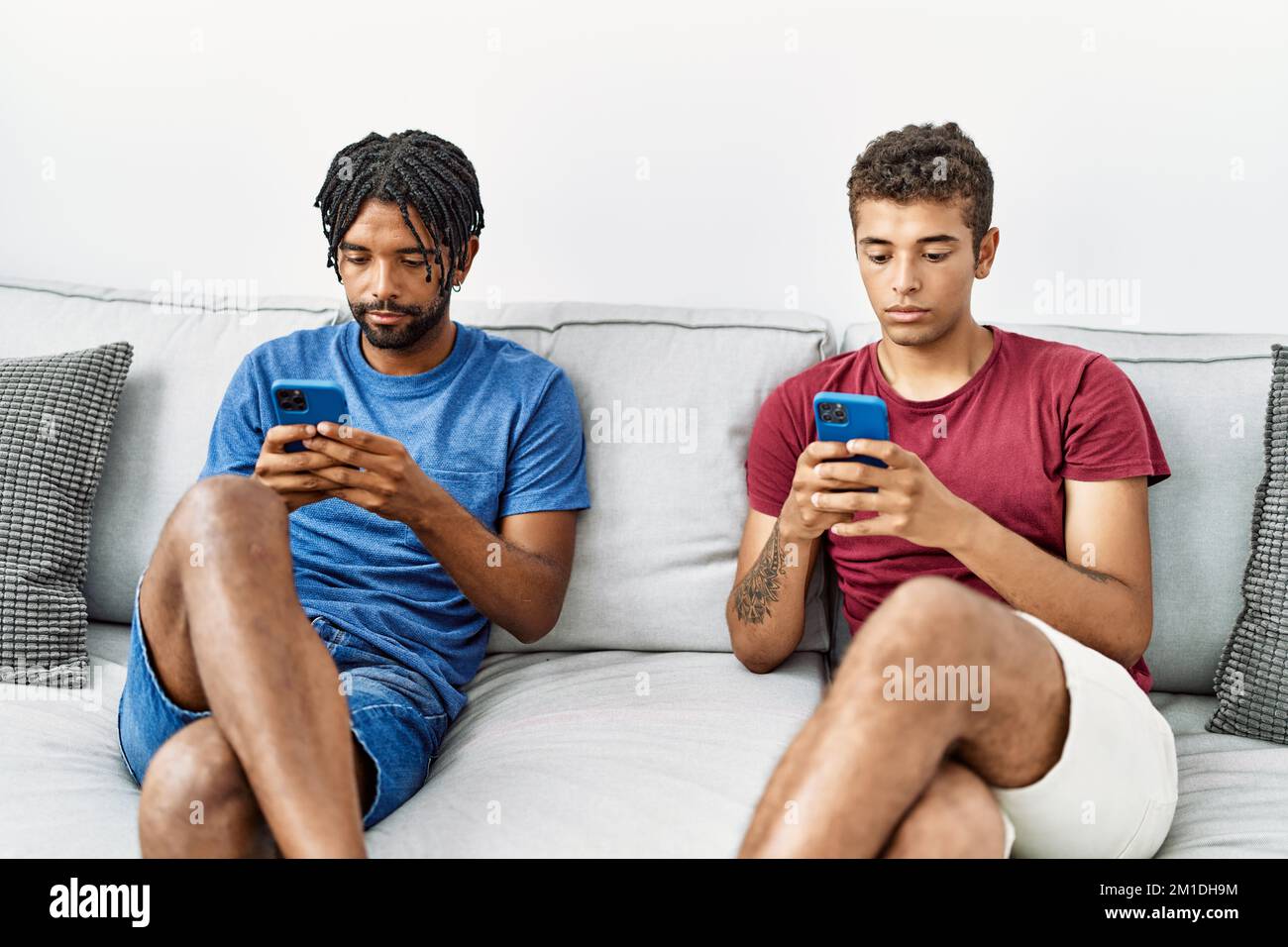 Two men friends using smartphone sitting on sofa at home Stock Photo