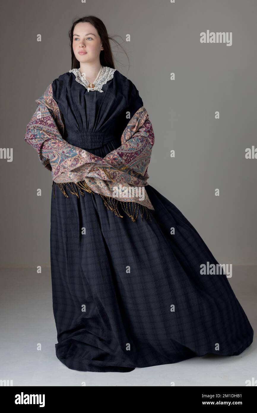 A young Victorian woman wearing a blue cotton dress with lace trim against a studio backdrop Stock Photo