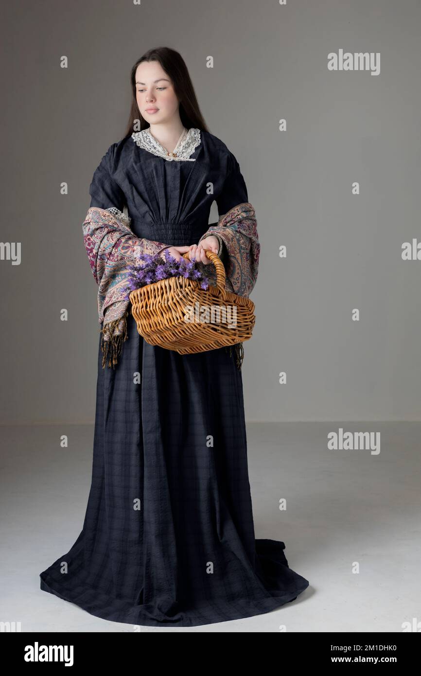 A young Victorian woman wearing a blue cotton dress with a paisley shawl and holding a basket of lavender Stock Photo