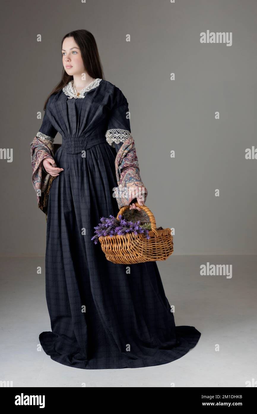 A young Victorian woman wearing a blue cotton dress with a paisley shawl and holding a basket of lavender Stock Photo