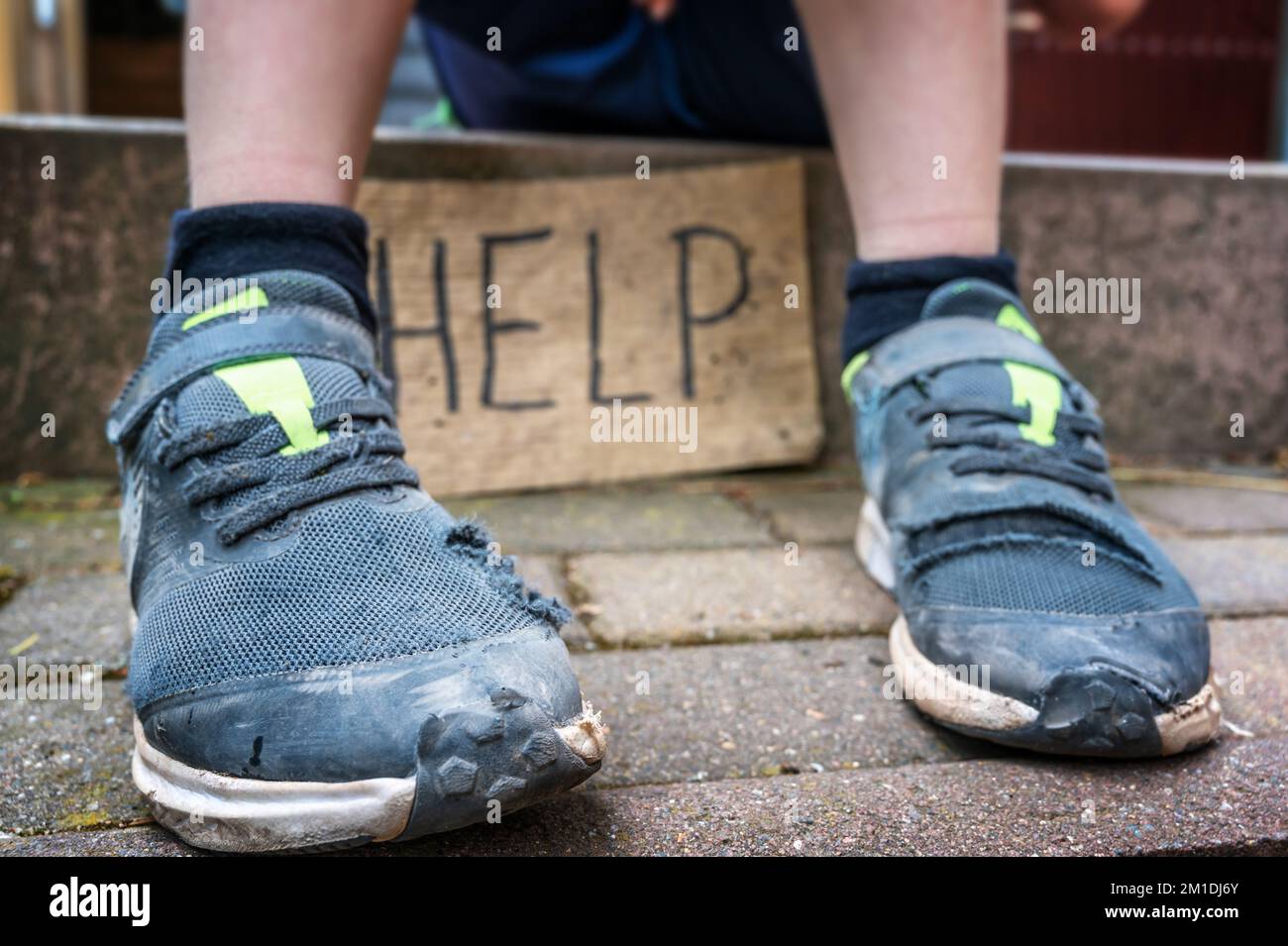 Child in broken shoes and a sign with the word Help in English Stock Photo