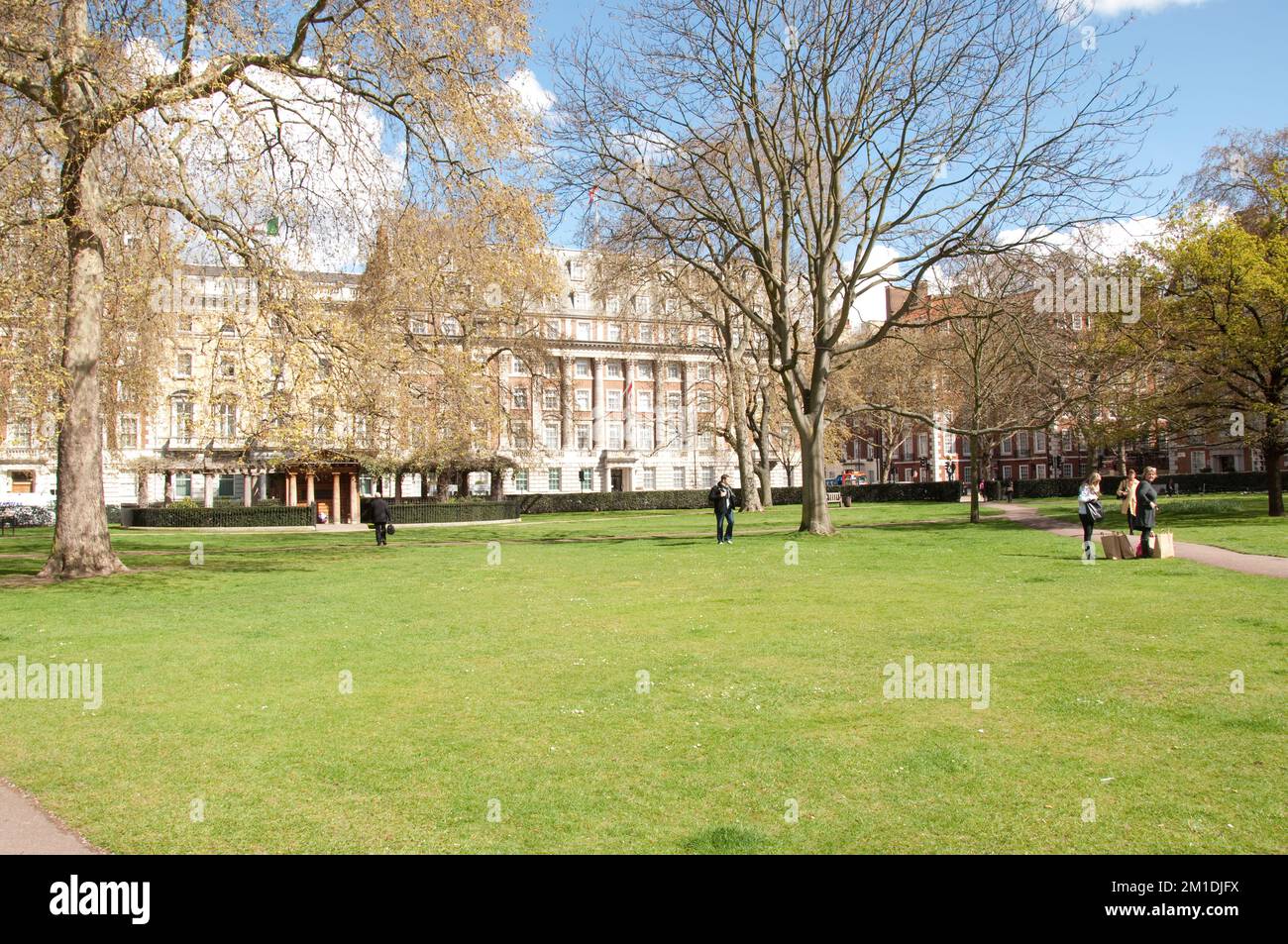 Gardens, Grosvenor Square, Mayfair, Westminster, London, UK - a few people in the garden, Canadian Embassy at far end. Stock Photo