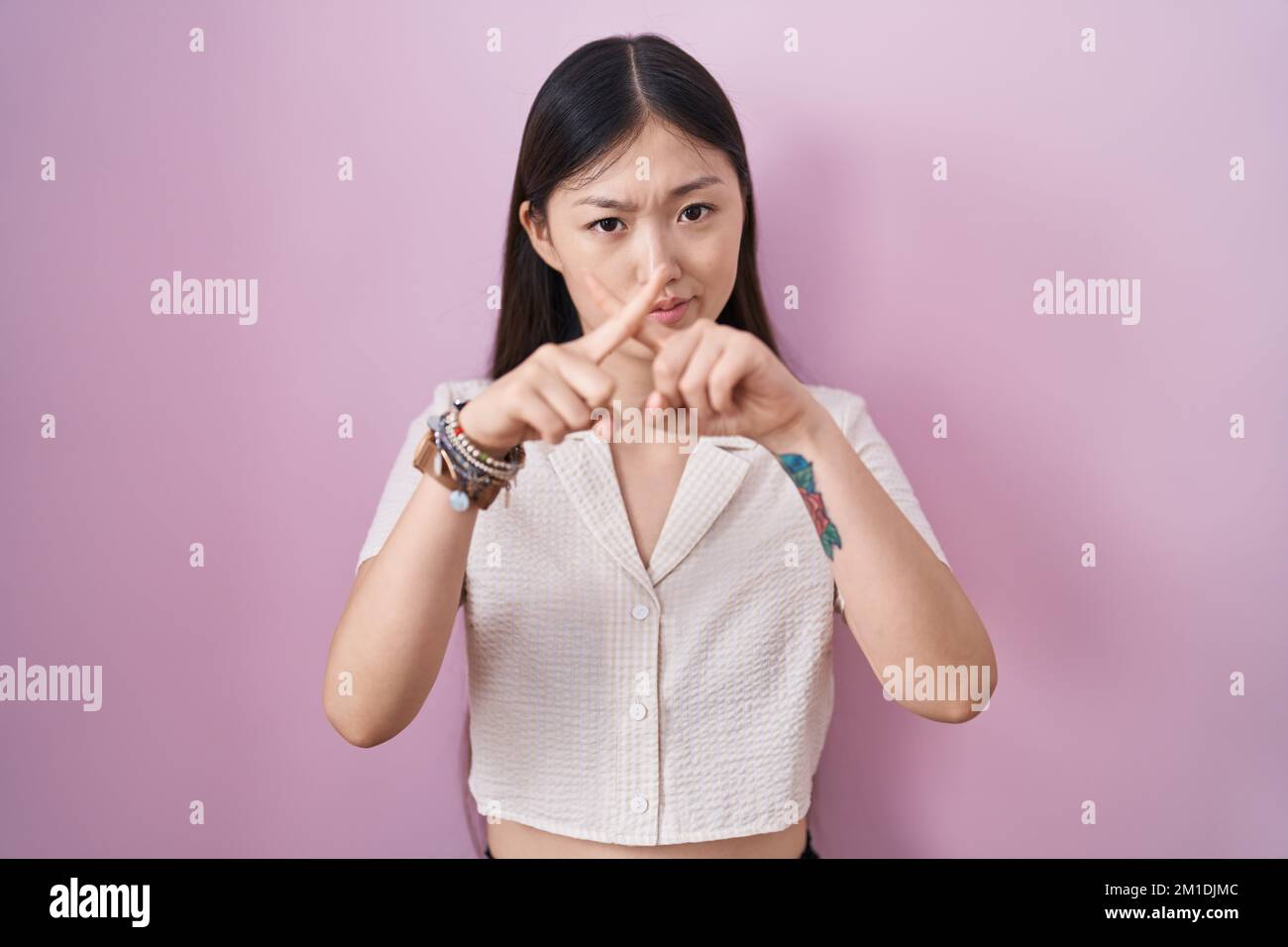 Chinese young woman standing over pink background rejection expression crossing fingers doing negative sign Stock Photo