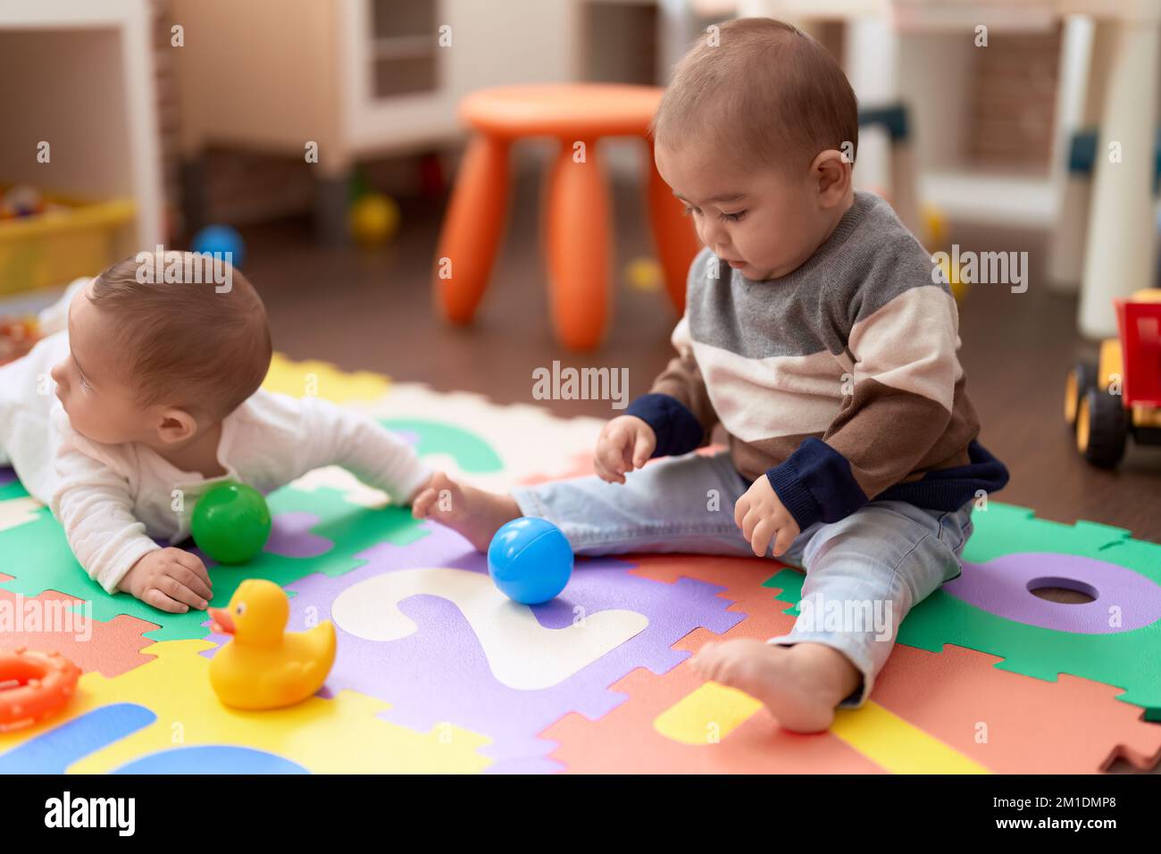 Two adorable toddlers playing with balls sitting on floor at kindergarten Stock Photo