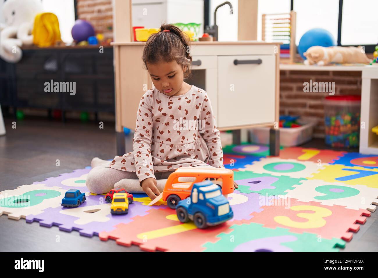 Adorable hispanic girl playing with car toy sitting on floor at ...
