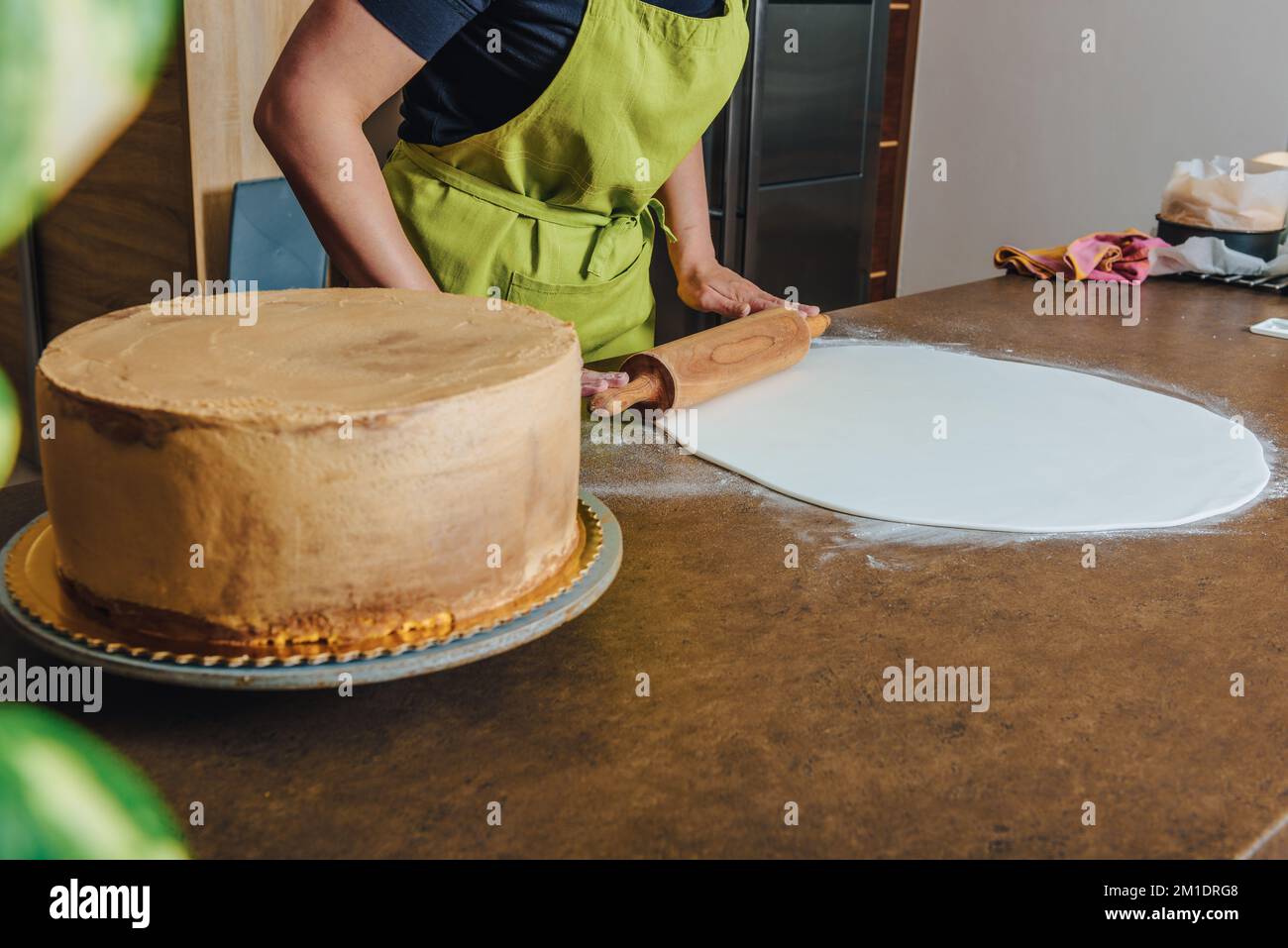 Woman using rolling pin preparing pink fondant for cake decorating, hands detail. DIY, sequence, step by step, part of series. Stock Photo