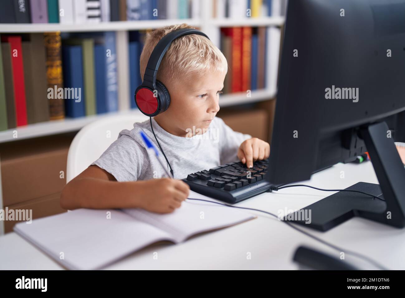 Adorable toddler student using computer writing on notebook at ...
