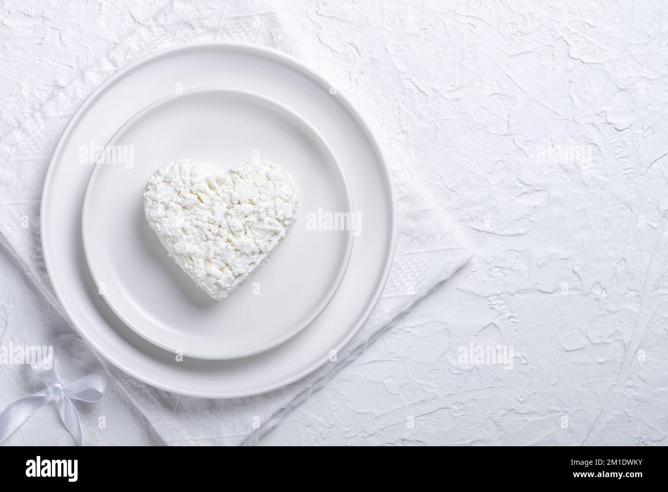 Heart shaped cottage cheese in a plate on a white table. Copy space for text Stock Photo