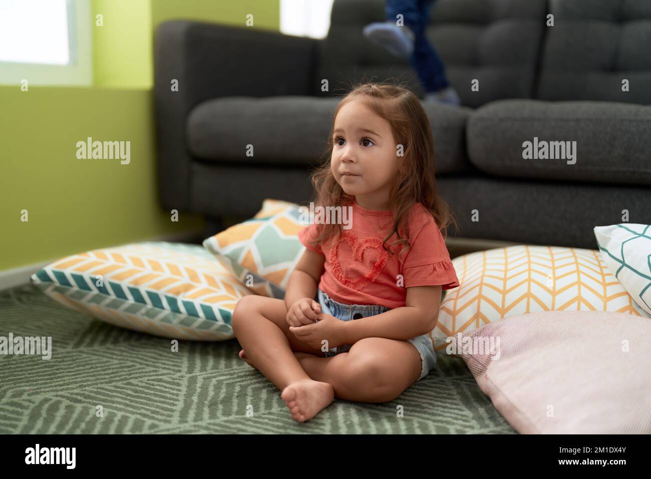 Adorable hispanic girl sitting on floor with relaxed expression at home ...