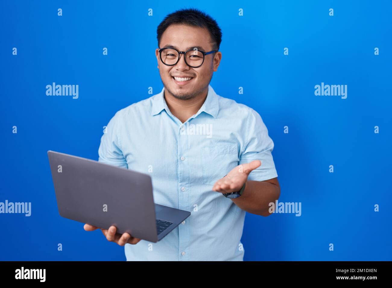 Chinese young man using computer laptop pointing aside with hands open ...