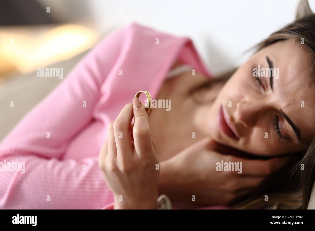 Sad fiancee looking at her engagement ring lying on a couch Stock Photo