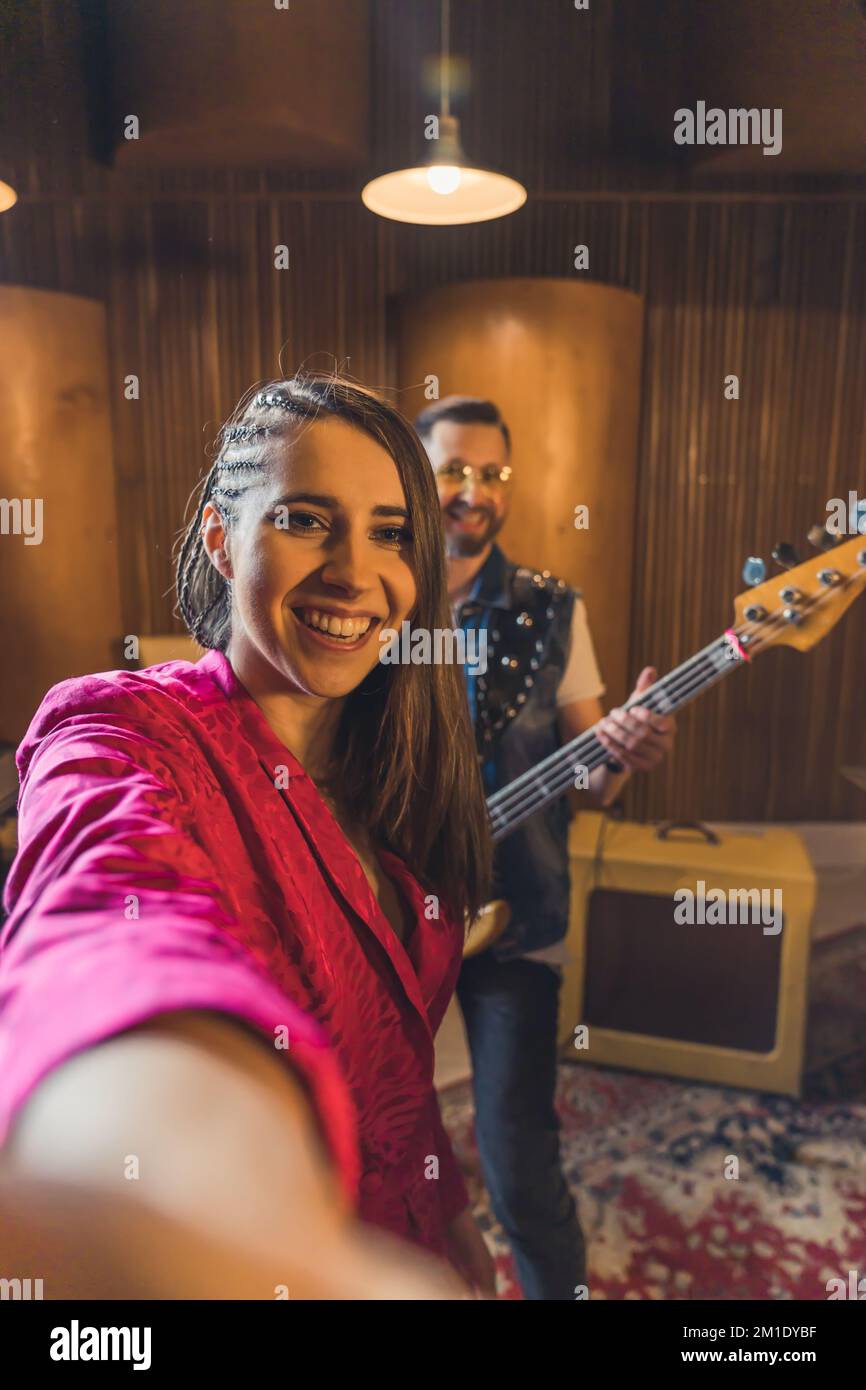 Happy brownhaired woman vocalist takes a selfie with male guitarist. Rock band practice before
