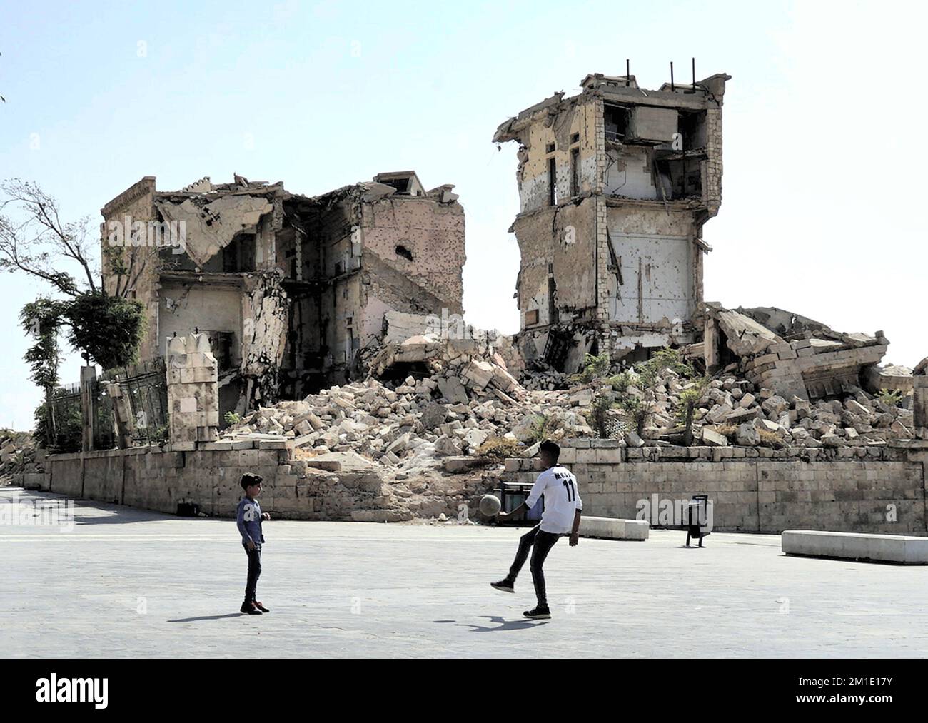 Two boys playing with a ball in the square in front of the citadel next to a destroyed Grand Serail government building, Aleppo, Syria Stock Photo