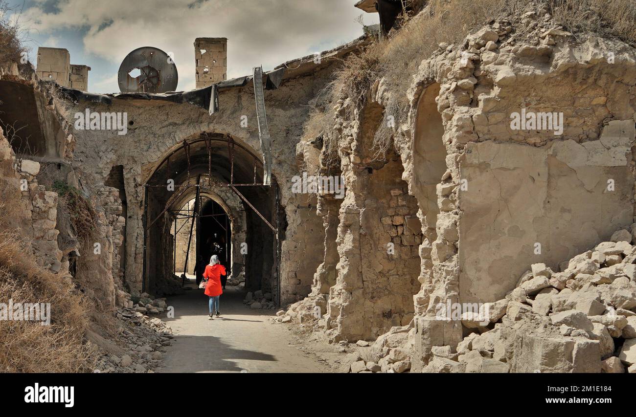A woman in a red cloak and hijab walking through the destroyed souk, Aleppo, Syria Stock Photo