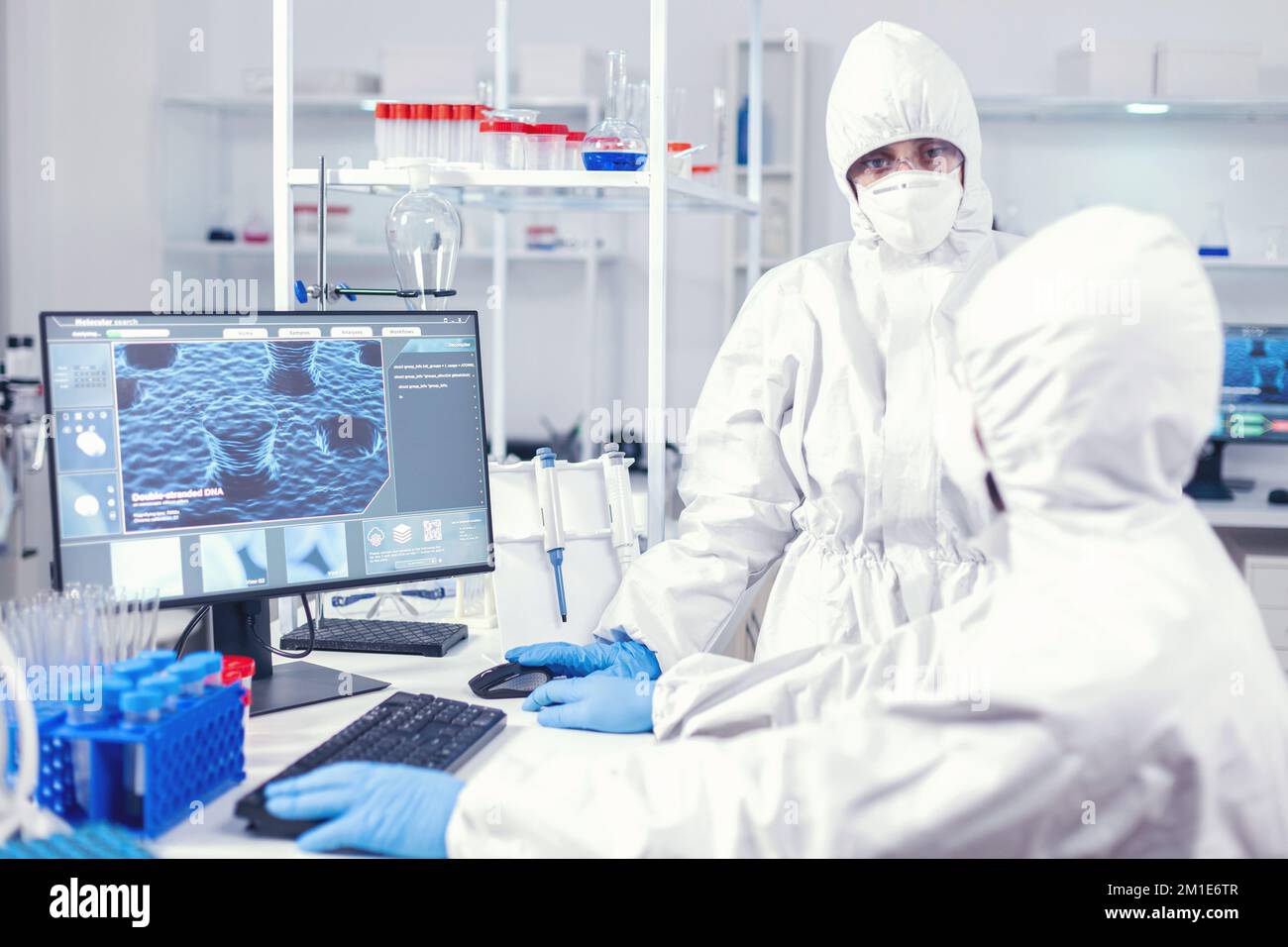 Nurse in protection suit discussing with lab technician dressed in Team