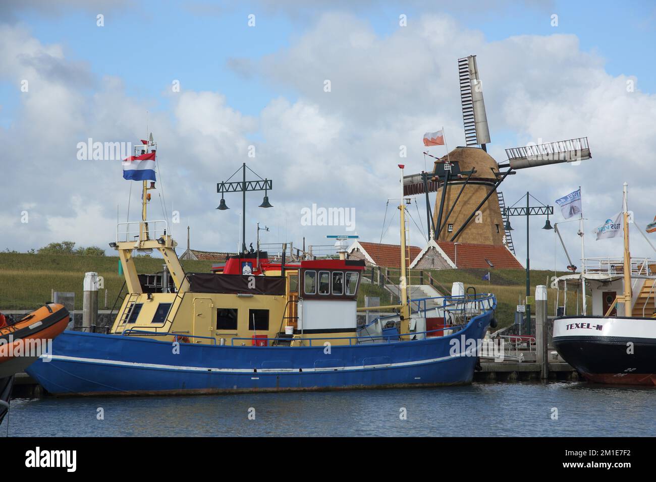 Harbour with ships at the quay wall and windmill in Oudeschild, Texel, Oudeschild, Texel, North Holland, Holland, Netherlands Stock Photo