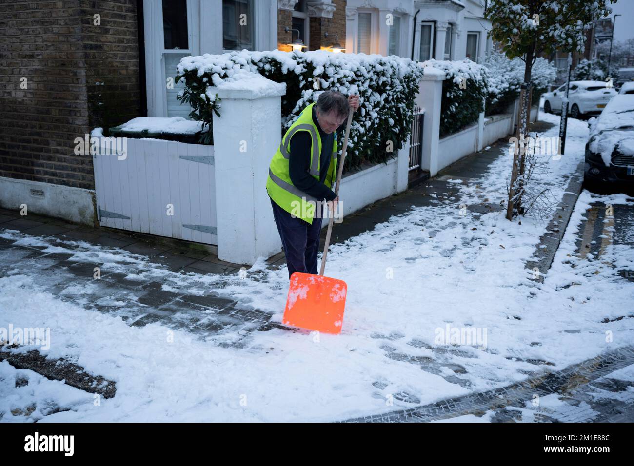 A community snow warden clears pavements outside residential properties after low temperatures and overnight snowfall on south London homes on Ruskin Park in SE24, on 12th December 2022, in London, England. Stock Photo