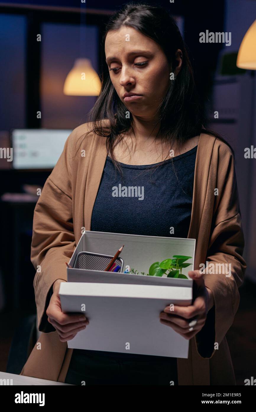 Desperate layed-off feeling stressed about job loss at workplace. Sad woman holding her belongings late at night in the office after being dismissed from job. Fired businesswoman, economy crisis Stock Photo