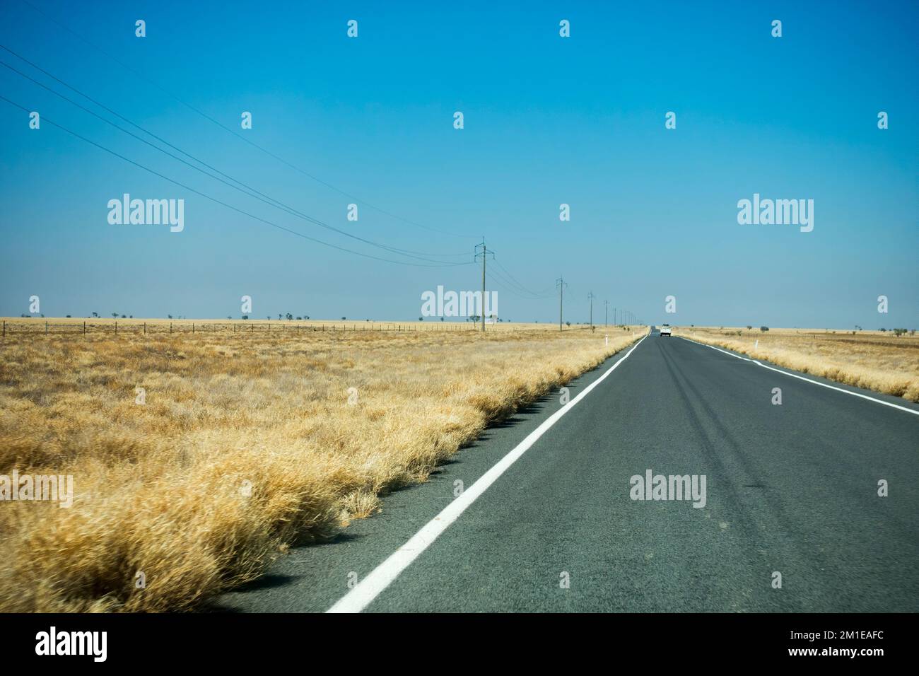 Long straight road near Corfield in rural Australia with dry grasss and