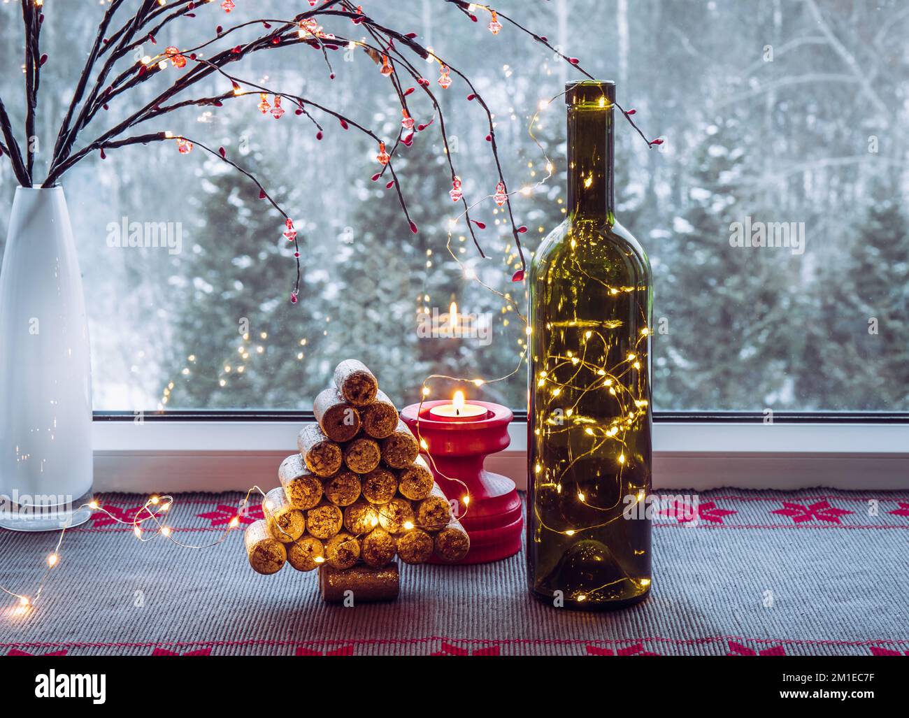 Christmas decoration set with wine bottle filled with micro led party lights and spruce tree made with used wine corks, behind is window with snowy. Stock Photo