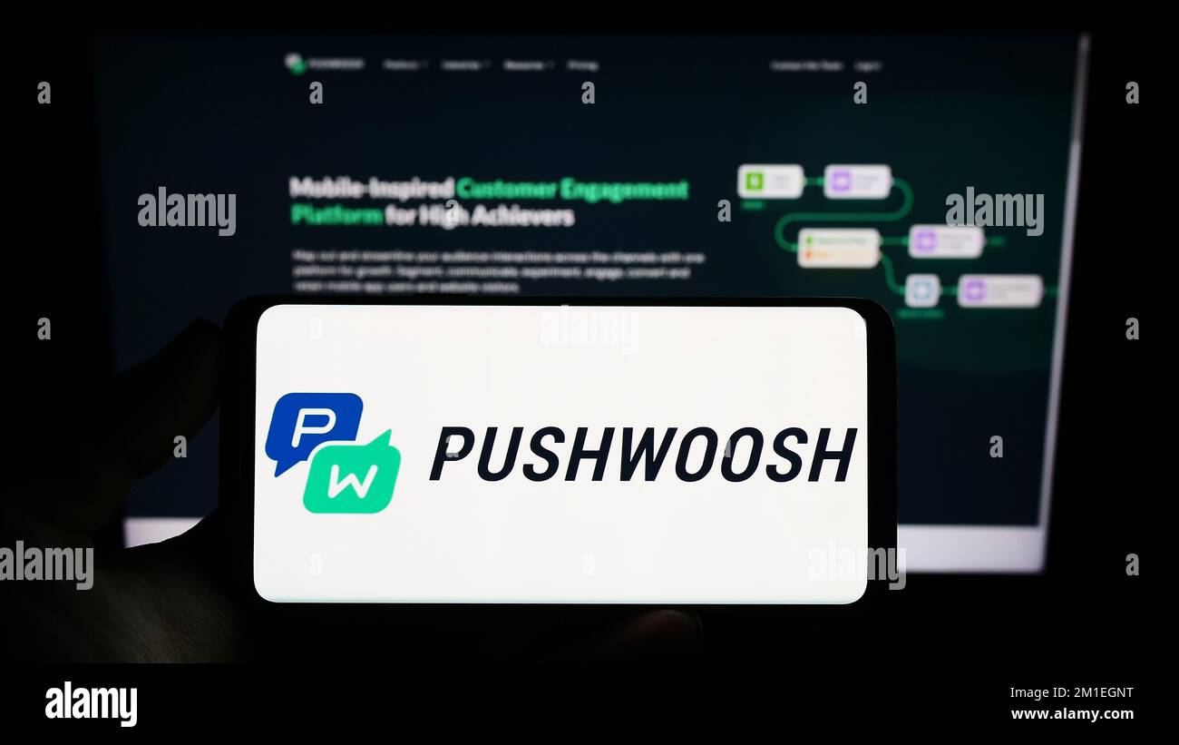 Person holding smartphone with logo of US marketing platform company Pushwoosh Inc. on screen in front of website. Focus on phone display. Stock Photo