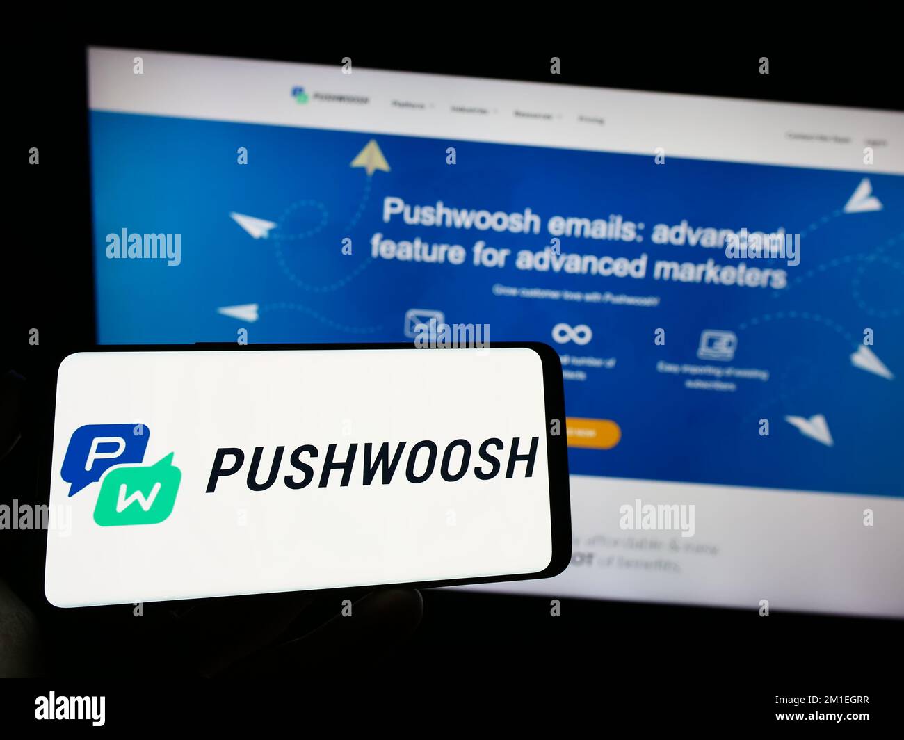 Person holding cellphone with logo of marketing platform company Pushwoosh Inc. on screen in front of business web page. Focus on phone display. Stock Photo