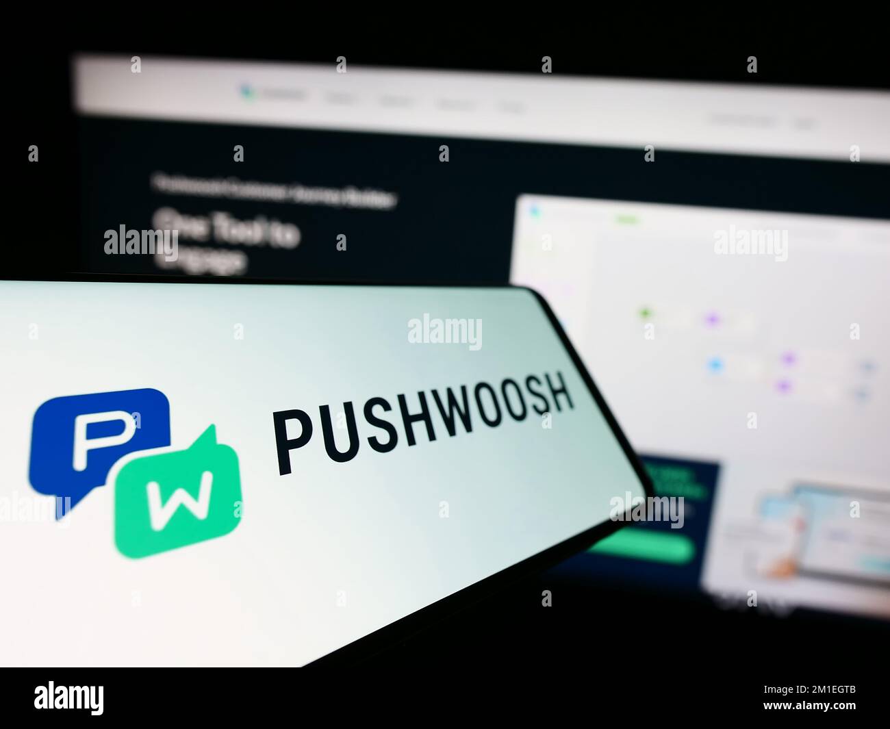 Mobile phone with logo of American marketing platform company Pushwoosh Inc. on screen in front of website. Focus on left of phone display. Stock Photo