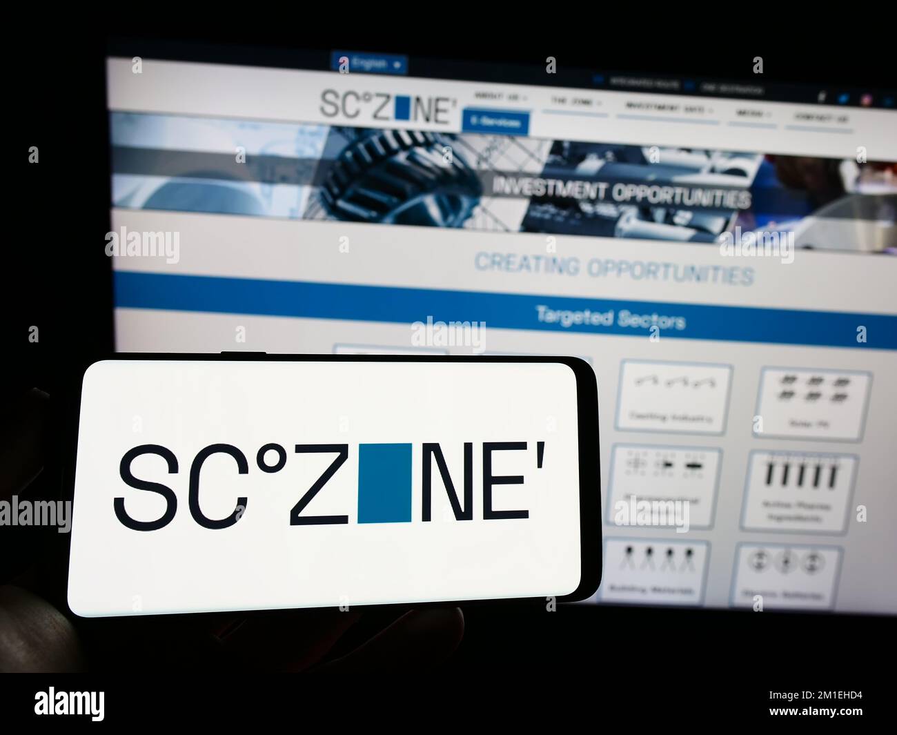 Person holding cellphone with logo of Egyptian Suez Canal Economic Zone (SCZONE) on screen in front of webpage. Focus on phone display. Stock Photo